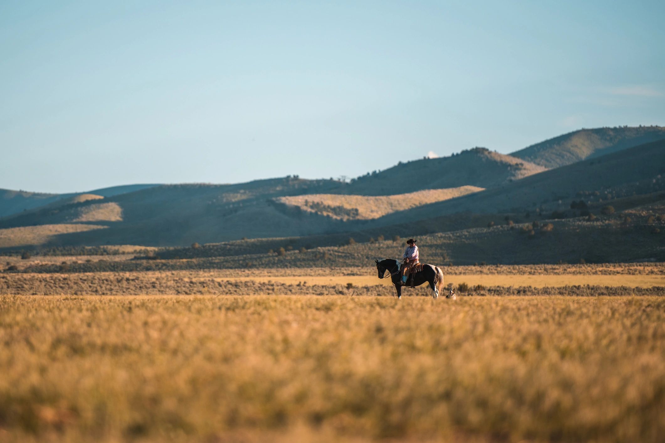 Cowboy riding horseback across open country with mountains in the distance