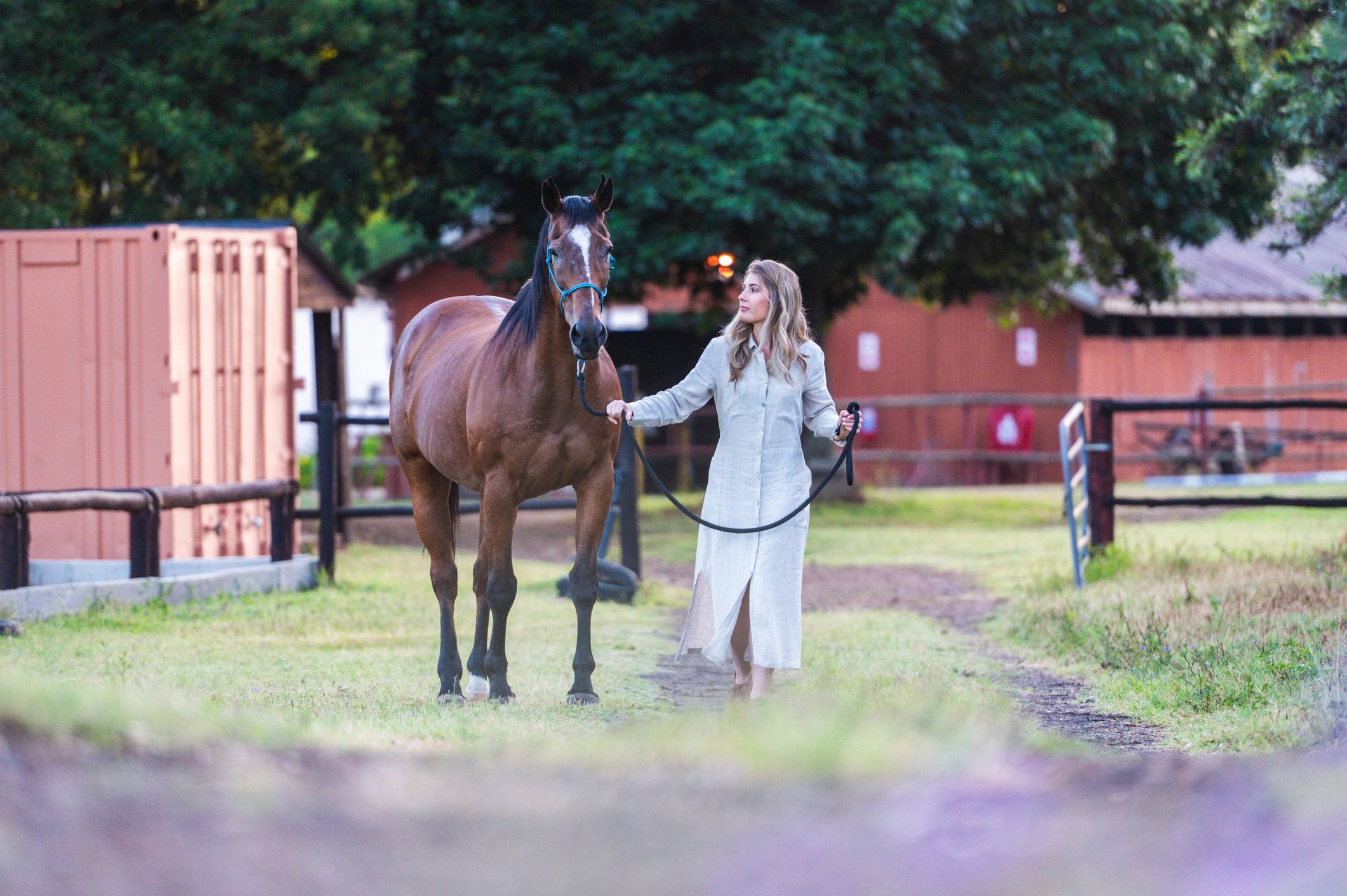 Rider leading a horse along a rustic stable path