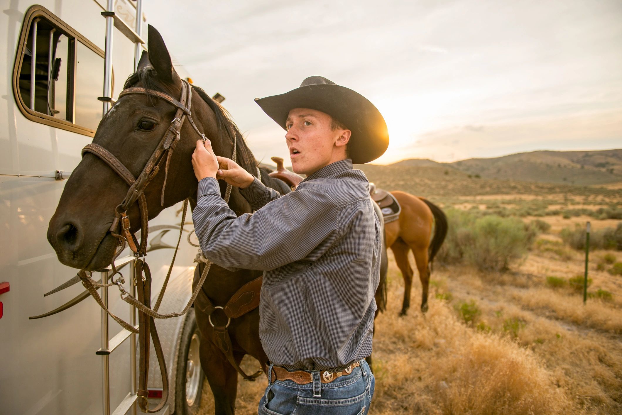 Cowboy preparing a horse to ride at sunset